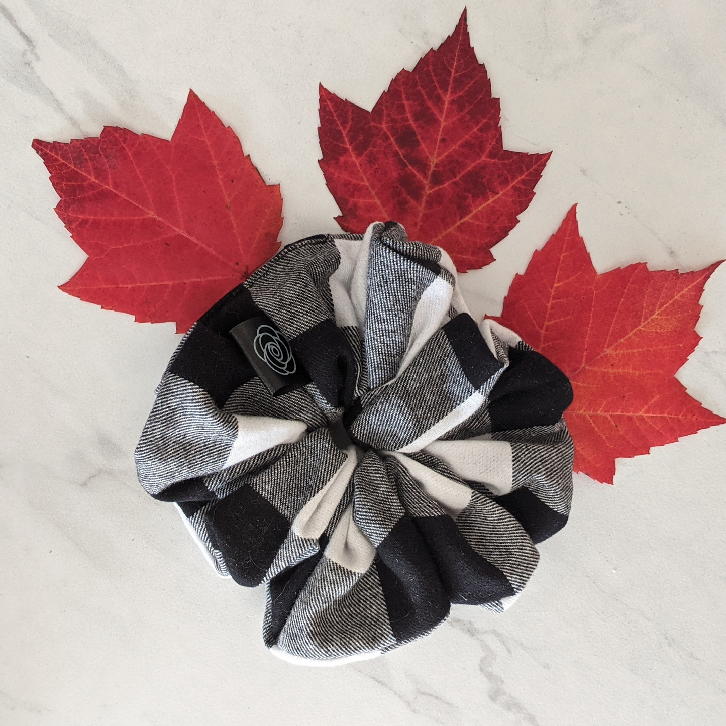 black and white flannel plaid scrunchie with a black tag made in Canada displayed with  red maple leafs