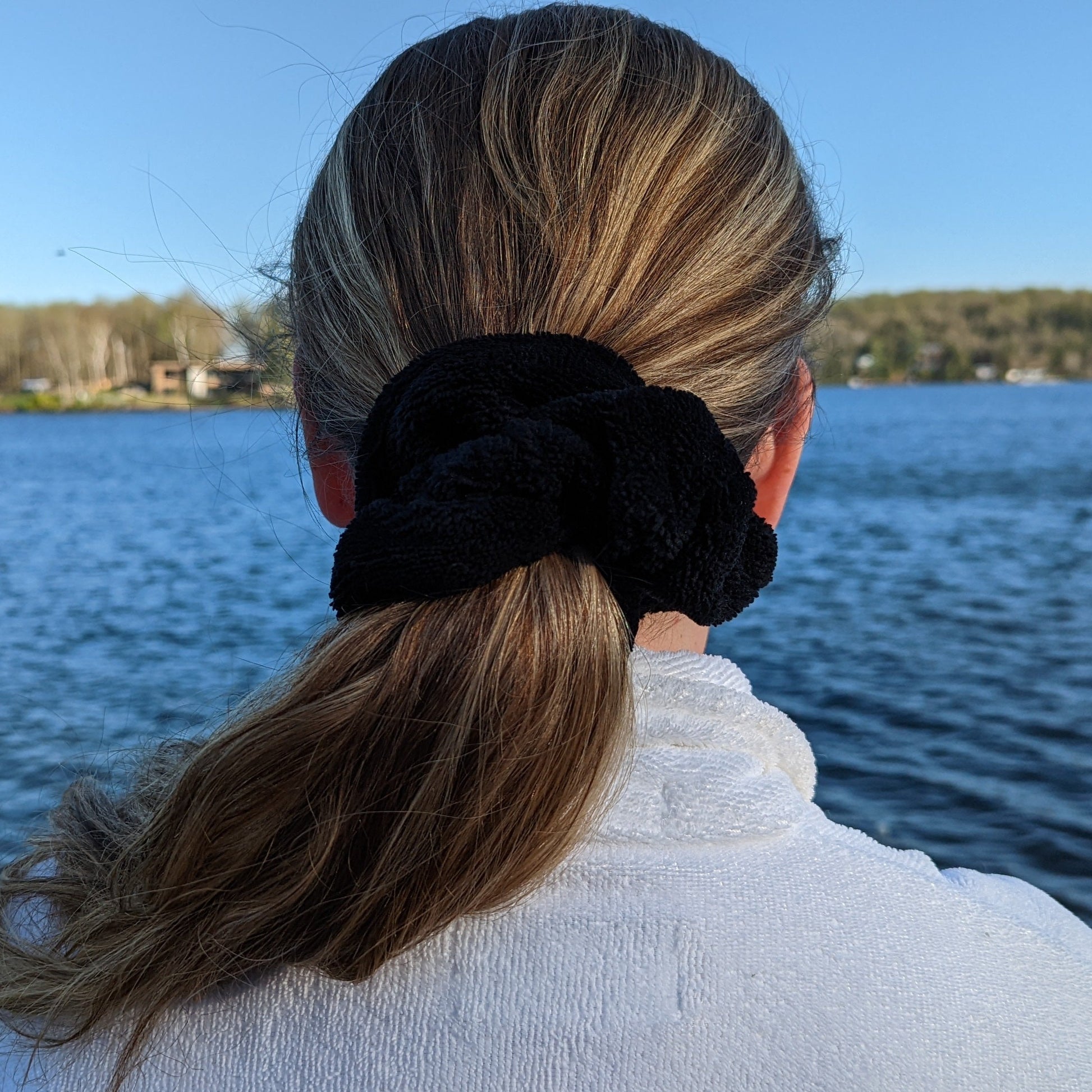black microfiber scrunchie tied in womens long hair, the lake in the background
